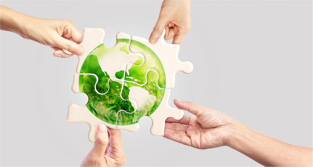 Four hands each holding a piece of a puzzle form a complete image of a green earth.