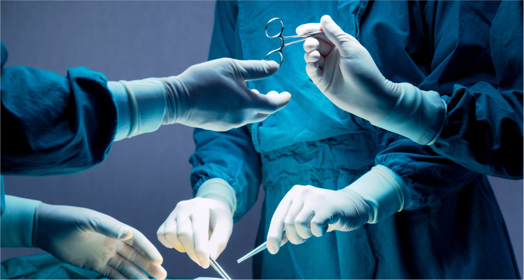 Surgeons wearing blue surgical gowns and gloves are performing a procedure, with one handing a surgical instrument to another.